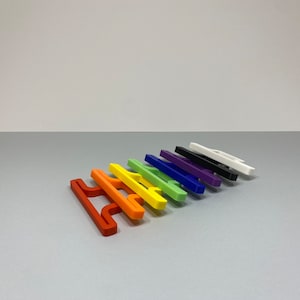 May include: A set of ten colourful plastic bag holders in various colours, including red, orange, yellow, green, blue, purple, black, and white. The holders are arranged in a row, with the red holder at the front and the white holder at the back.