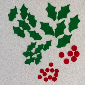 May include: A collection of green felt holly leaves and red felt berries. The holly leaves are arranged in a cluster, while the berries are scattered around them.