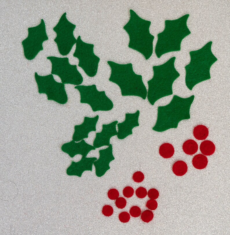 May include: A collection of green felt holly leaves and red felt berries. The holly leaves are arranged in a cluster, while the berries are scattered around them.