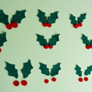 May include: Nine felt holly sprigs with red felt berries. The sprigs are various sizes and are arranged in a row on a light green background.