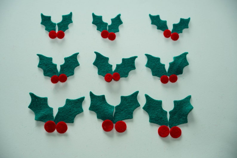 May include: Ten felt holly sprigs with red berries. Each sprig has two green leaves and two red berries.