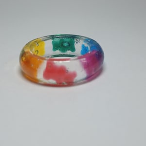 May include: A clear resin ring with embedded colorful gummy bears. The ring is a rainbow of colors, including red, orange, yellow, green, blue, and purple.