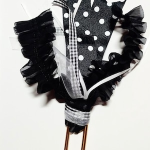 May include: A decorative paper clip featuring a collection of black and white ribbons. The ribbons include polka dots, ruffles, and a checkered pattern. The paper clip is gold-colored.