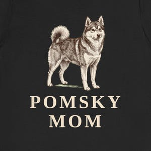 May include: A black short-sleeved t-shirt featuring a detailed illustration of a Pomsky dog standing in profile. Below the dog, the text POMSKY MOM is printed in a light beige, sans-serif font. The shirt has a crew neckline and a standard fit.