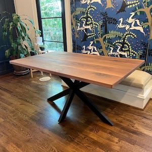 May include: A rectangular wooden table with a natural finish and black metal legs. The table has a modern design and is set on a hardwood floor. The table's dimensions are approximately 72 inches long and 36 inches wide.