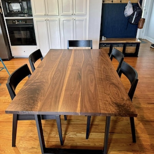 May include: A dark wood dining table with a black metal frame. The table has a natural wood grain pattern and is surrounded by four black chairs.