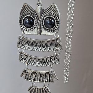May include: Silver-toned owl pendant necklace. The owl pendant features black stone eyes and intricate geometric patterns. The necklace has a delicate chain and a decorative, layered design, perfect for adding a unique touch to any outfit.
