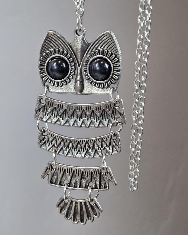 May include: Silver-toned owl pendant necklace. The owl pendant features black stone eyes and intricate geometric patterns. The necklace has a delicate chain and a decorative, layered design, perfect for adding a unique touch to any outfit.