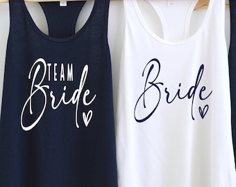 May include: Three tank tops with the text "Team Bride" and "Bride" in white and blue lettering. The tank tops are navy blue and white.