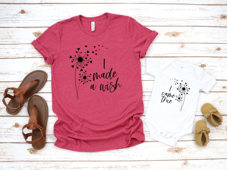 May include: A red t-shirt and white onesie with matching dandelion graphics and text. The t-shirt says "I made a wish" and the onesie says "I came true". Brown sandals and baby shoes are also in the image.