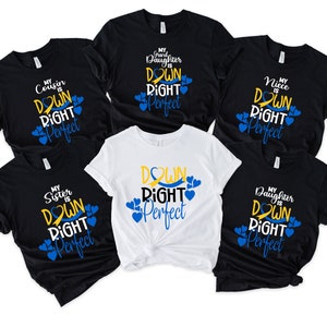 May include: A collection of five short-sleeved t-shirts, four black and one white, each featuring the text "Down Right Perfect" with a blue and yellow awareness ribbon and blue hearts. The shirts display various family titles including Cousin, Granddaughter, Niece, Sister, and Daughter.