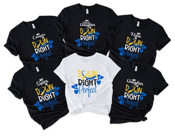 Könnte beinhalten: Sechs schwarze T-Shirts mit weißem Text und blauen und gelben Akzenten. Der Text auf den Shirts lautet "Mein [Familienmitglied] ist Down Right Perfect". Die Shirts sind in einem Kreis angeordnet, wobei ein weißes T-Shirt in der Mitte liegt. Der Text auf dem weißen T-Shirt lautet "Down Right Perfect".
