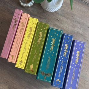May include: A set of seven Harry Potter books with spines in various colours. The spines are pink, peach, yellow, green, teal, blue, and purple. Gold lettering and illustrations feature on each spine, displaying the title and volume number.