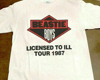 May include: White t-shirt with a black and red diamond logo that says "Beastie Boys" and the text "Licensed to Ill Tour 1987".