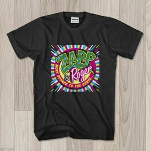 May include: Black t-shirt featuring a colorful graphic design. The design includes the words "Zapp & Roger" in green and pink, surrounded by a vibrant array of colors and the text "More Bounce to the Ounce..."