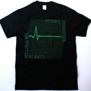 Może przedstawiać: Czarny T-shirt z zielonym nadrukiem przedstawiającym EKG na siatce. Tekst "LIFE IS KILLING ME" znajduje się po lewej stronie grafiki, a "TYPE O NEGATIVE" po prawej.