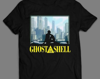 May include: Black t-shirt with a yellow graphic of a cityscape and a person sitting on a rooftop. The text "Ghost in the Shell" is printed in yellow below the graphic.
