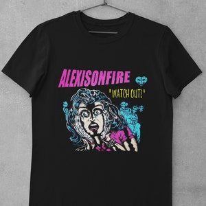 Könnte beinhalten: Schwarzes T-Shirt mit einem Grafikdruck einer Frau mit einem schockierten Ausdruck, umgeben von Skeletten. Der Text "ALEXISONFIRE" und "WATCH OUT!" ist auf dem T-Shirt aufgedruckt.