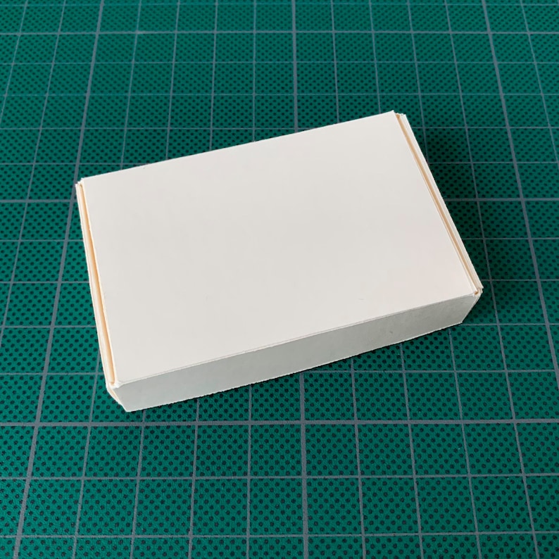 May include: A white cardboard box with a plain surface. The box is sitting on a green cutting mat.