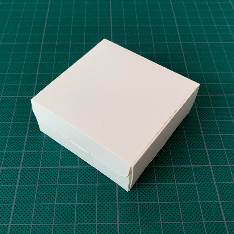 May include: A white cardboard box with a square shape and folded edges.