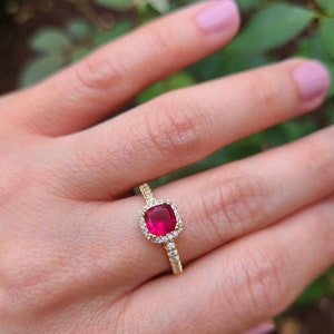 Puede incluir: Un anillo de oro con una piedra preciosa roja rodeada de piedras blancas más pequeñas.