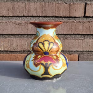May include: A ceramic vase with a bulbous body and a narrow neck. The vase is decorated with a colorful floral pattern in shades of blue, red, yellow, and brown.