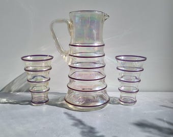 May include: A set of three iridescent glass pieces with purple stripes. The set includes a pitcher and two glasses.
