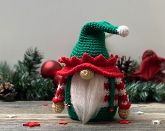 May include: A crocheted gnome wearing a green hat with a white pom-pom, a red and white striped sweater, and a white beard. The gnome is sitting on a wooden surface with red and white stars.