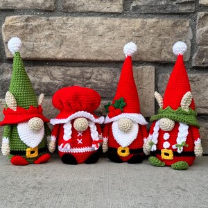 Four festive crochet Christmas gnomes posed in front of a stone background, featuring Santa, Mrs. Claus, and two elf gnomes in red, green, and white outfits with belts, hats, and holiday details, handmade amigurumi figures shown for the downloadable PDF crochet pattern by CrochetGnomeMania.