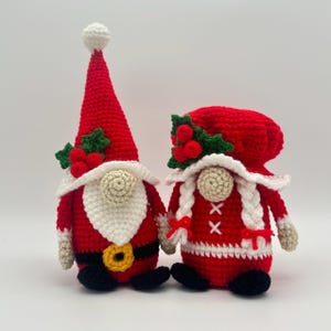 Crochet Santa and Mrs. Claus gnomes in red and white Christmas outfits decorated with holly leaves and berries, handmade amigurumi figures shown for the downloadable PDF crochet pattern.