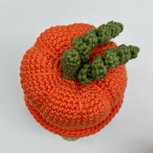 Top view of a round, orange crocheted pumpkin featuring a textured, with green stem and veins.