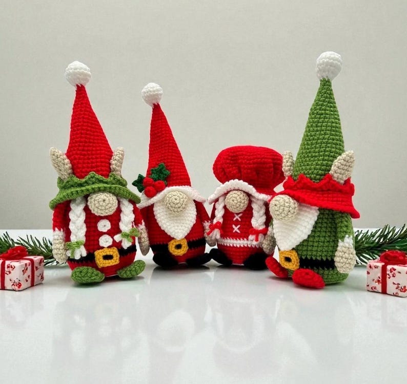 Four festive crochet Christmas gnomes displayed on a white surface with small wrapped gifts and pine branches, including Santa, Mrs. Claus, and two elf gnomes in red, green, and white outfits, handmade amigurumi figures featured for the downloadable PDF crochet pattern.