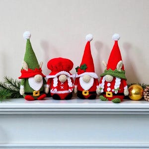 Four crochet Christmas gnomes displayed on a white mantel with pine branches, pinecones, and a gold ornament, featuring Santa, Mrs. Claus, and two elf gnomes in red, green, and white outfits, handmade amigurumi figures shown for the downloadable PDF crochet pattern.
