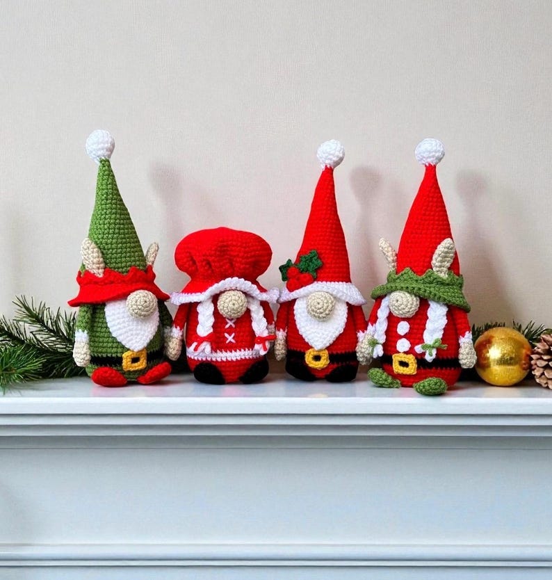 Four crochet Christmas gnomes displayed on a white mantel with pine branches, pinecones, and a gold ornament, featuring Santa, Mrs. Claus, and two elf gnomes in red, green, and white outfits, handmade amigurumi figures shown for the downloadable PDF crochet pattern.