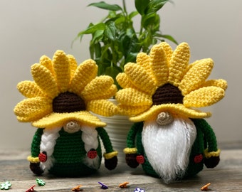May include: Two crocheted gnome ornaments with sunflower hats. The gnomes are wearing green outfits and have white beards. The sunflowers are yellow with brown centers.