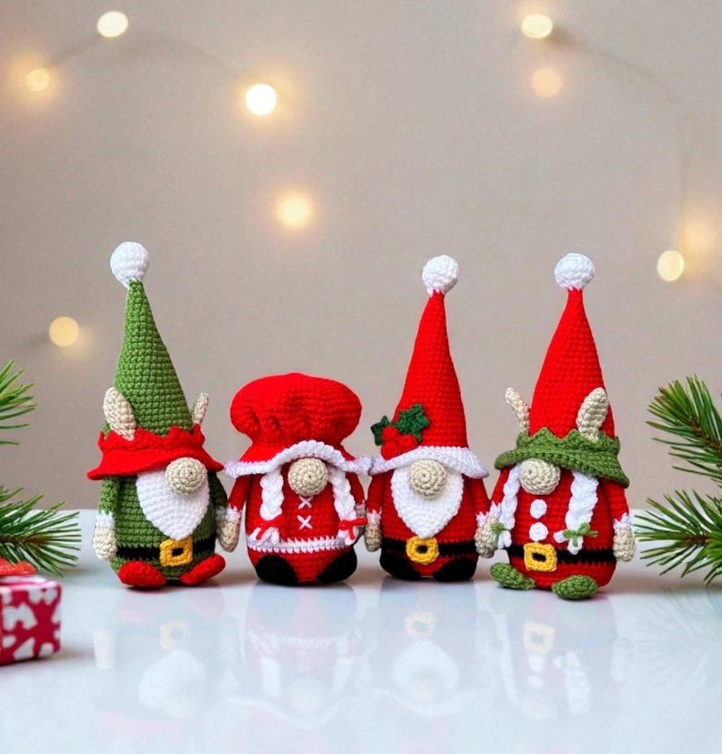 Four festive crochet Christmas gnomes posed on a white surface with soft twinkling holiday lights and pine branches in the background, including Santa, Mrs. Claus, and two elf gnomes in red, green, and white outfits, handmade amigurumi figures featured for the downloadable PDF crochet pattern.