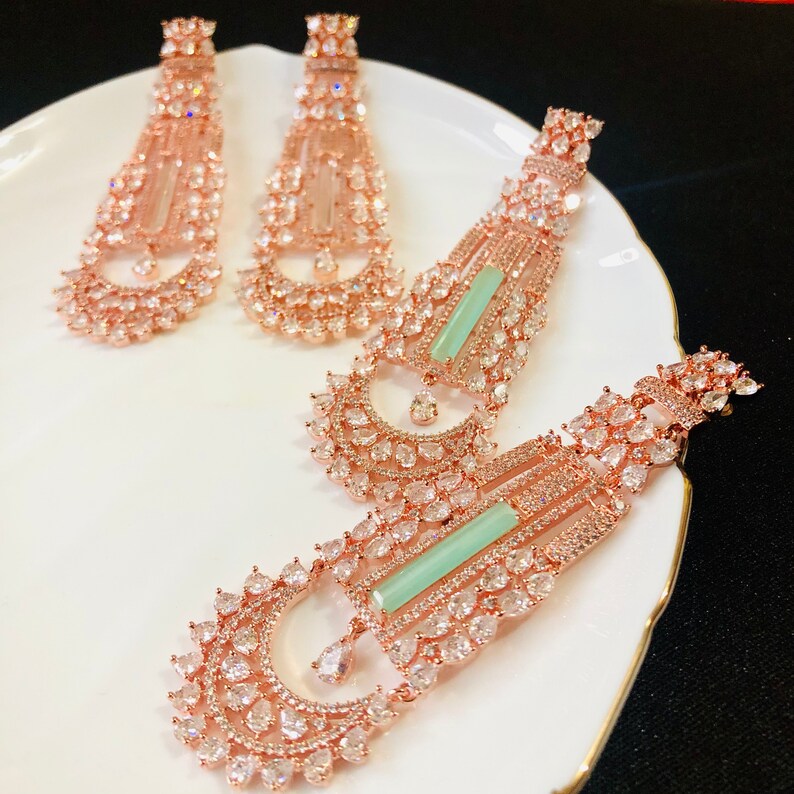 Puede incluir: Un par de pendientes de oro rosa con una piedra verde y piedras de circonita c&uacute;bica transparentes. Los pendientes son largos y colgantes.