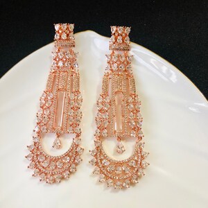 Puede incluir: Un par de pendientes colgantes de oro rosa con un dise&ntilde;o geom&eacute;trico y piedras de circonita c&uacute;bica transparentes.