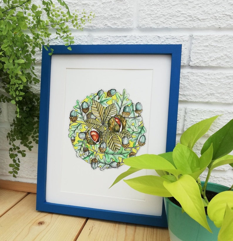 May include: A framed print of a watercolour illustration of a circle of oak leaves and acorns. The leaves are green and brown, and the acorns are light blue and brown. The background is yellow.