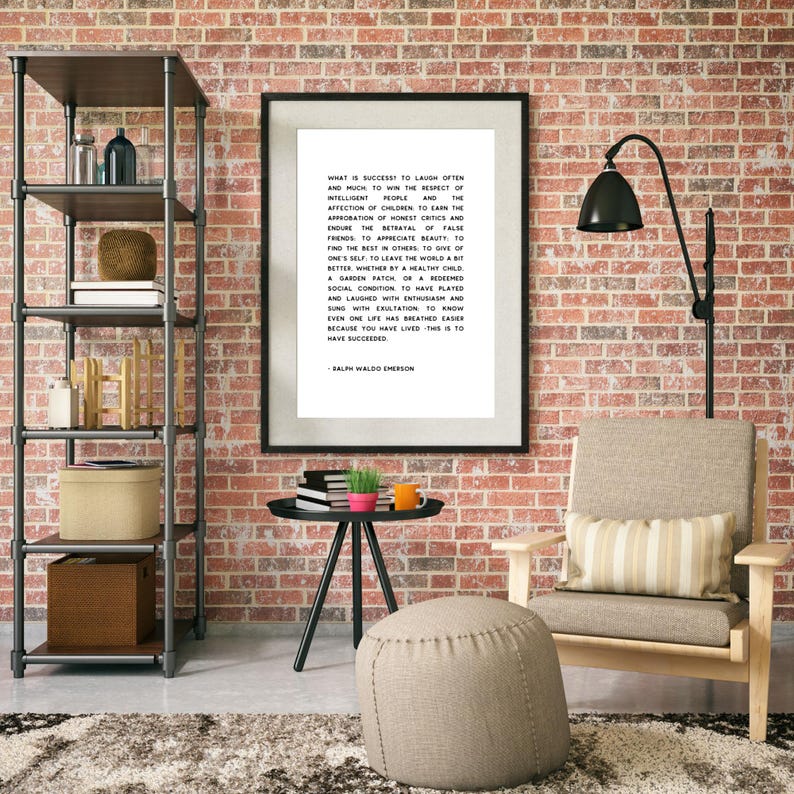 May include: A framed print with a black border, featuring text by Ralph Waldo Emerson, hangs on a brick wall. The room includes a metal shelf, a chair with a striped pillow, a small table, and a footstool. A black lamp is positioned near the chair.