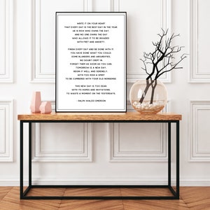 Puede incluir: Impresi&oacute;n tipogr&aacute;fica en blanco y negro con una cita de Ralph Waldo Emerson sobre vivir en el momento presente. La impresi&oacute;n est&aacute; enmarcada y colgada en una pared blanca sobre una mesa de madera con un jarr&oacute;n de ramas.