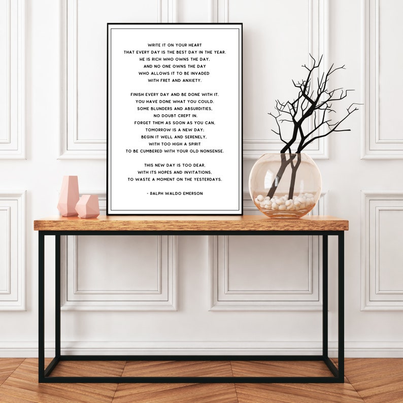 Puede incluir: Impresi&oacute;n tipogr&aacute;fica en blanco y negro con una cita de Ralph Waldo Emerson sobre vivir en el momento presente. La impresi&oacute;n est&aacute; enmarcada y colgada en una pared blanca sobre una mesa de madera con un jarr&oacute;n de ramas.