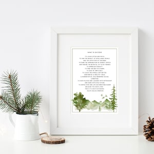 Op de afbeelding: Een ingelijst afdruk met een groene aquarel achtergrond met een bergketen en bomen. De afdruk bevat een citaat van Ralph Waldo Emerson over succes, dat luidt: "Vaak en veel lachen... Dat is succesvol zijn."