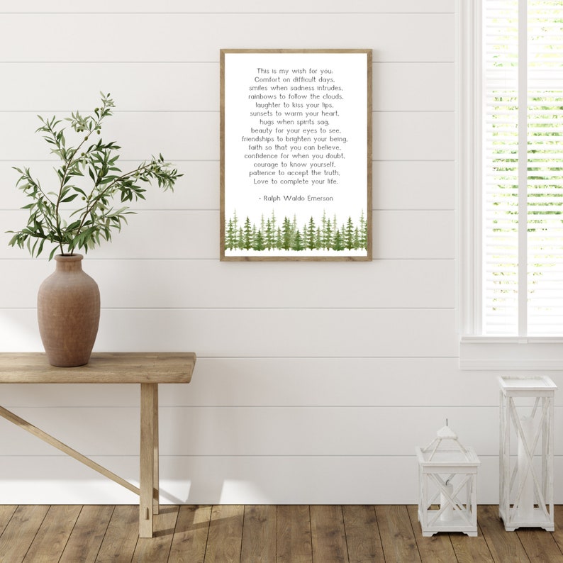 May include: A framed print with a wooden frame displays a poem by Ralph Waldo Emerson. The text is in black font on a white background, with a watercolor forest design at the bottom. The print is displayed on a wooden table with a vase of greenery.