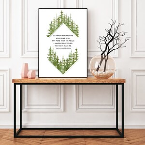 May include: A white framed print featuring a green watercolour forest design and a quote by Ralph Waldo Emerson: "I cannot remember the books I've read any more than the meals I have eaten: even so. They have made me." The print is displayed on a wooden table with a vase of branches and two pink ceramic vases.
