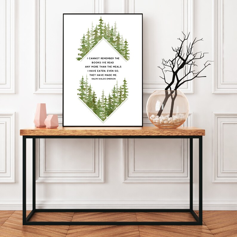 May include: A white framed print featuring a green watercolour forest design and a quote by Ralph Waldo Emerson: "I cannot remember the books I've read any more than the meals I have eaten: even so. They have made me." The print is displayed on a wooden table with a vase of branches and two pink ceramic vases.