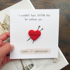 May include: A white anniversary card with the text "I wouldn't have COTTON this far without you..." and "HAPPY 2nd ANNIVERSARY". The card features a red yarn heart pierced by two black needles.