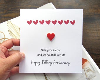 May include: A white card with a red heart and nine smaller red hearts. The card reads "Nine years later and we're still kiln it! Happy Pottery Anniversary."