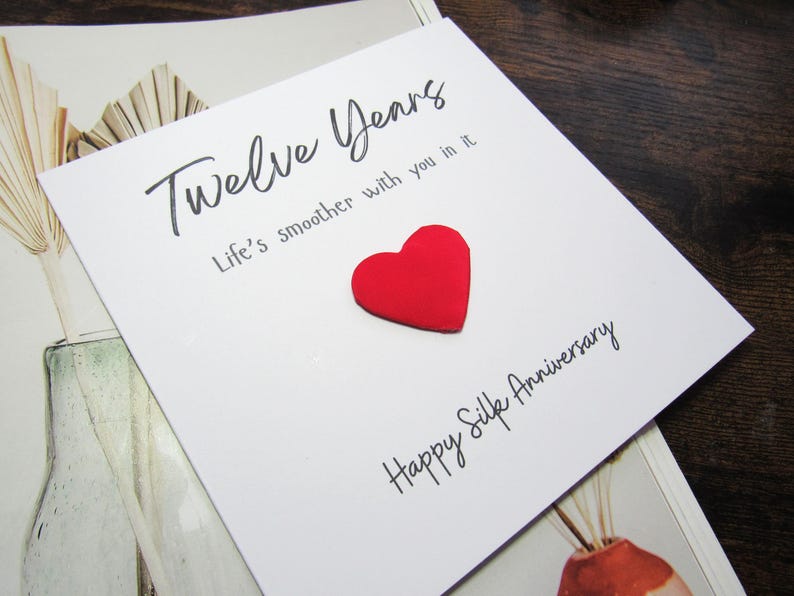 K&ouml;nnte beinhalten: Eine wei&szlig;e Gru&szlig;karte mit den Worten "Twelve Years" und "Life's smoother with you in it" in schwarzer Schrift. Ein erhabenes rotes Herz befindet sich in der Mitte der Karte. Darunter steht "Happy Silk Anniversary".