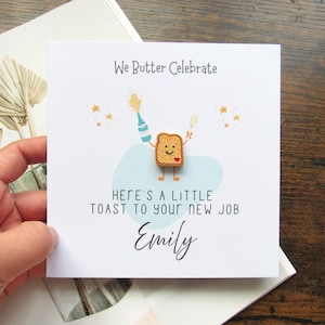 Può includere: Biglietto di auguri quadrato con il testo "We Butter Celebrate" e "Here's a little toast to your new job". La carta presenta un personaggio di toast dei cartoni animati con una faccia sorridente, che tiene in mano una bottiglia e dei bicchieri di champagne. Il nome "Emily" è scritto sotto.